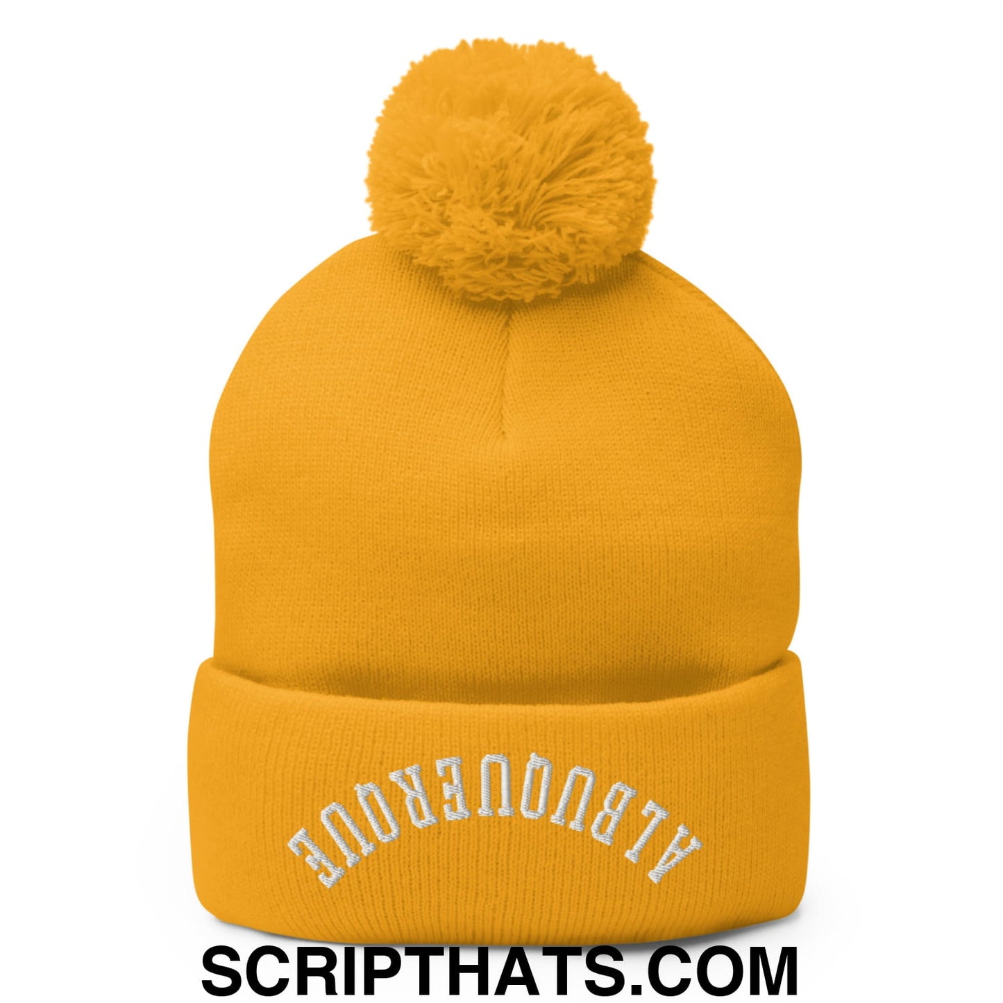 A mustard-yellow knit beanie with a fluffy pom-pom and white embroidered text on the cuff
