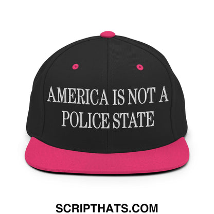 Black snapback hat with vibrant pink brim and button featuring white embroidered america is not a police state text