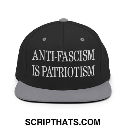 Black snapback cap with gray brim and white embroidered anti-fascism is patriotism text flat bill brim design