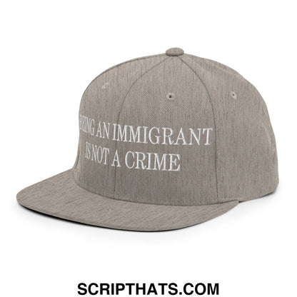 Gray flat bill brim snapback hat with white embroidered text being an immigrant is not a crime