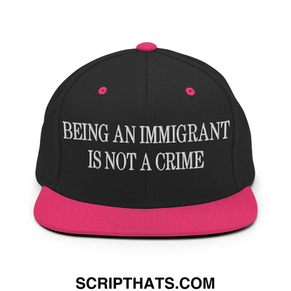 Black snapback cap with vibrant pink brim and button featuring white embroidered text being an immigrant is not a crime