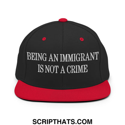 Black snapback cap with red brim and button featuring white embroidered text being an immigrant is not a crime