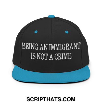 Black snapback hat with teal brim and button featuring white embroidered text being an immigrant is not a crime