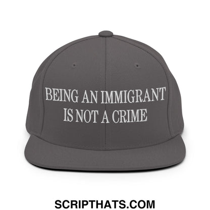 Gray snapback hat with white embroidered text reading being an immigrant is not a crime on the front panel