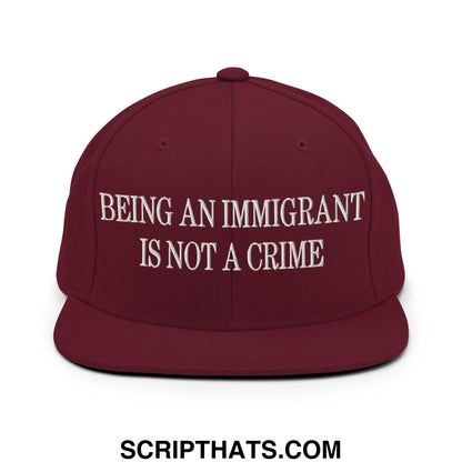 Maroon flat bill brim snapback hat with white embroidered text being an immigrant is not a crime