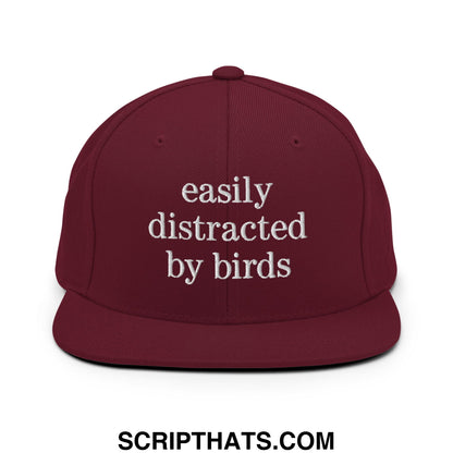 Maroon snapback hat with white embroidered easily distracted by birds text on a flat bill brim design