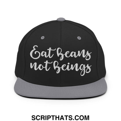 Black snapback cap with gray brim and button featuring white embroidered eat beans not beings text in cursive script