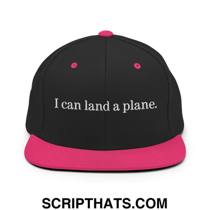 Black snapback cap with a vibrant pink brim and white embroidered i can land a plane text flat bill brim design