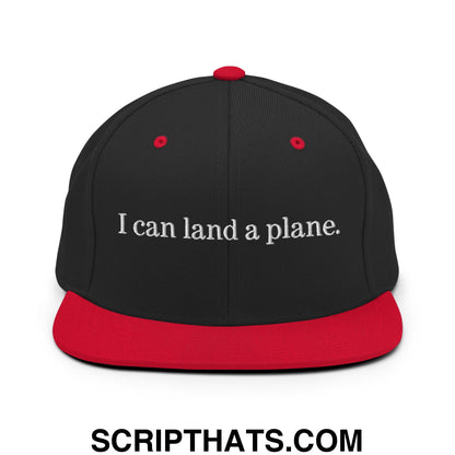 Black snapback cap with red brim and button featuring white embroidered text i can land a plane on front