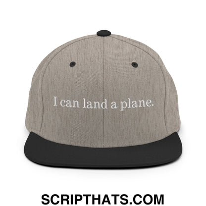 Gray and black snapback cap with white embroidered text reading ’i can land a plane.’