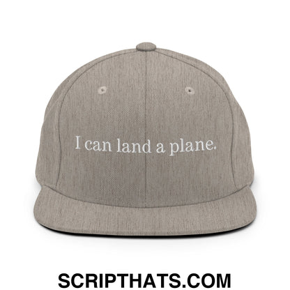 A gray heathered snapback cap with white embroidered text i can land a plane flat bill brim design