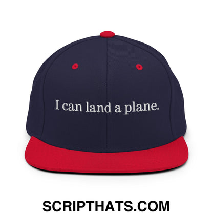 Navy blue snapback hat with red brim and button featuring white embroidered text i can land a plane