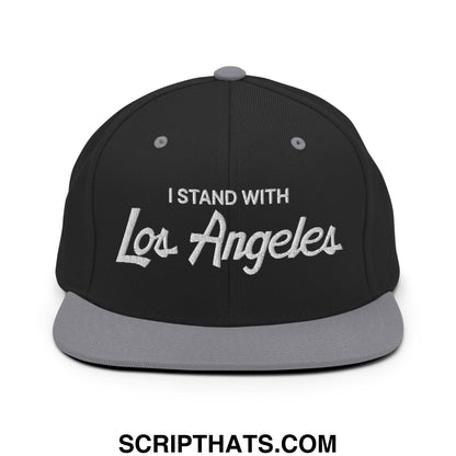 Black snapback cap with gray brim and white embroidered i stand with los angeles vintage sports script text