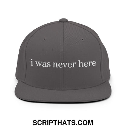 A dark gray snapback hat with white embroidered i was never here text and a flat bill brim design