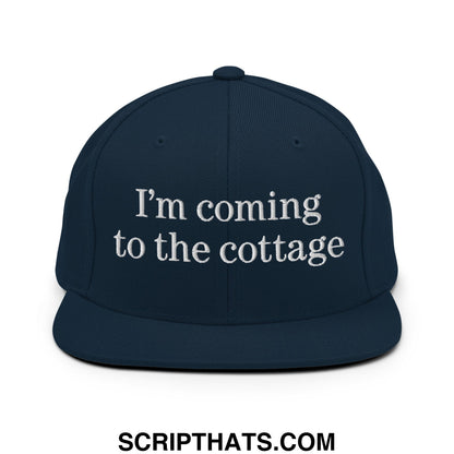 Navy blue snapback hat with white embroidered im coming to the cottage text and flat bill brim design