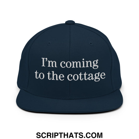 Navy blue snapback hat with white embroidered im coming to the cottage text and flat bill brim design