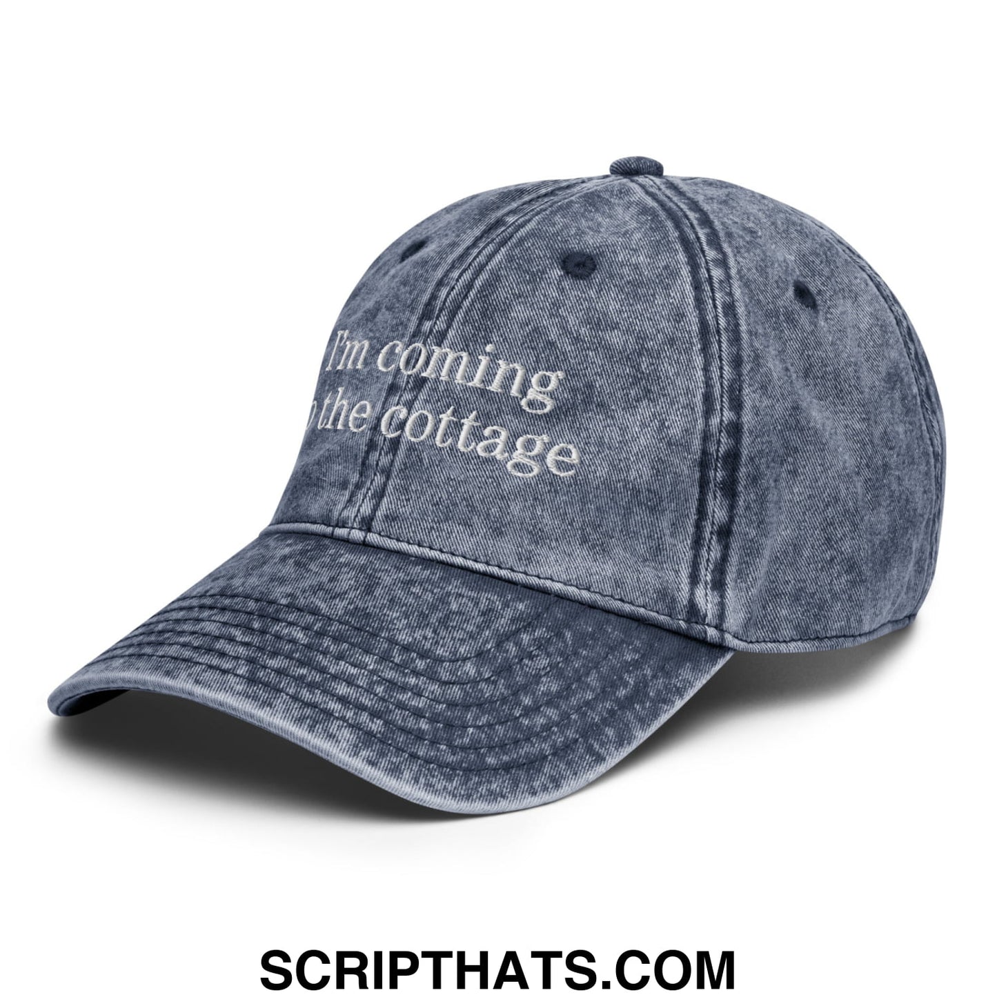 A faded denim unstructured dad hat embroidered with im coming to the cottage in white thread