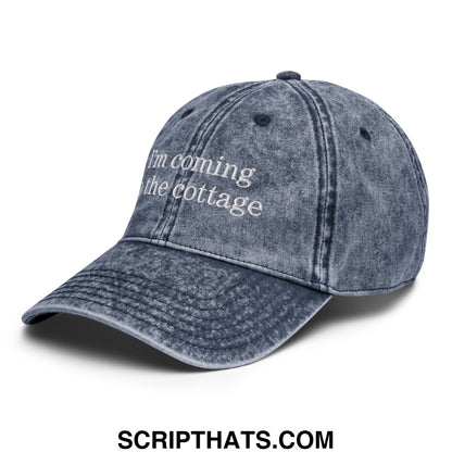 A faded denim unstructured dad hat embroidered with im coming to the cottage in white thread