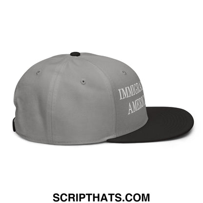 Gray and black snapback cap with immigrant america embroidered in white script on the side in flat brim style