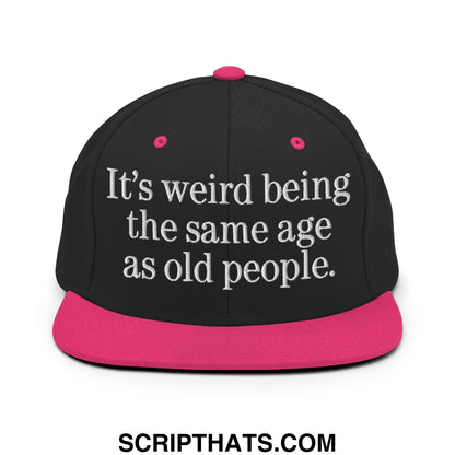 Black snapback hat with vibrant pink flat brim and white embroidered text it’s weird being the same age as old people