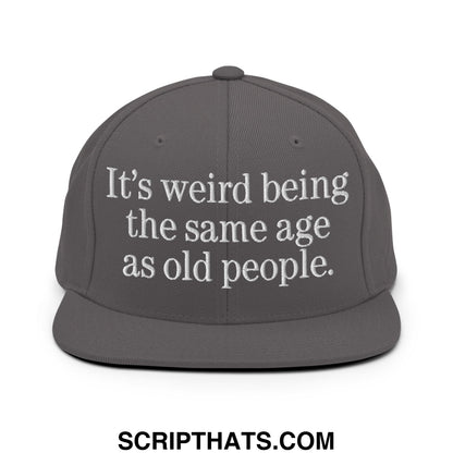 Gray embroidered flat bill snapback hat with white text reading its weird being the same age as old people