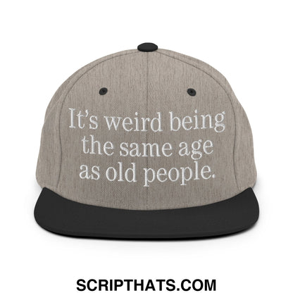 Gray snapback hat with black flat bill brim and embroidered white text reading its weird being the same age as old people