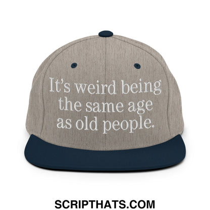Gray and navy blue snapback hat with white embroidered text it’s weird being the same age as old people flat bill brim