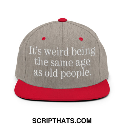 Gray snapback hat with red flat bill and white embroidered text it’s weird being the same age as old people