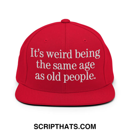 Red flat bill snapback hat with white embroidered text reading its weird being the same age as old people