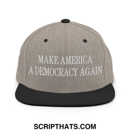 Gray snapback hat with black brim featuring embroidered white text make America a democracy again on the front