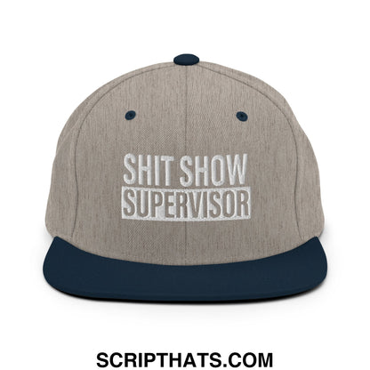 A gray and navy blue snapback hat with shit show supervisor embroidered in white on a flat bill brim