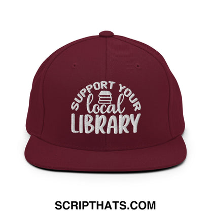 Maroon snapback hat with white embroidered support your local library text and stack of books graphic on the front