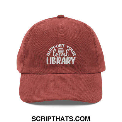 A rust-colored corduroy unstructured dad hat with white embroidered support your local library text and book icon