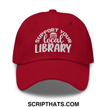 A red embroidered unstructured dad hat with support your local library text and a small stack of books icon above local