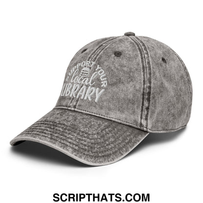 A faded gray denim dad hat with white embroidered support your local library text and a small library icon