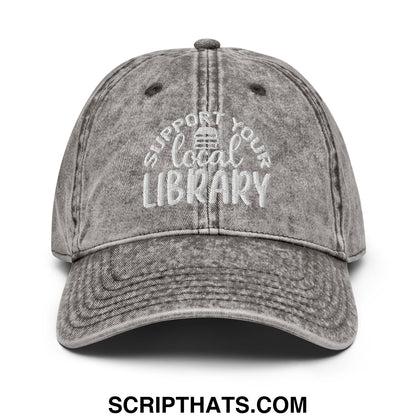 A faded gray unstructured denim dad hat with white embroidered text support your local library and a library icon