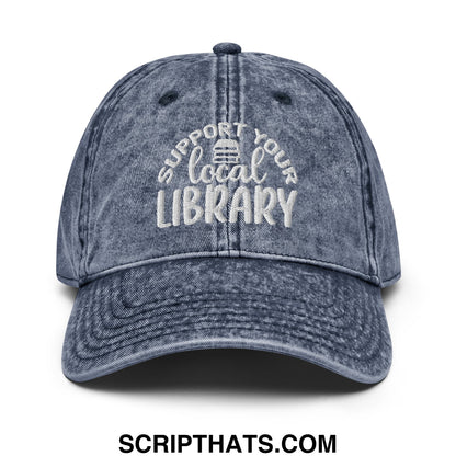 A faded blue denim dad hat with white embroidered support your local library text and a small library icon