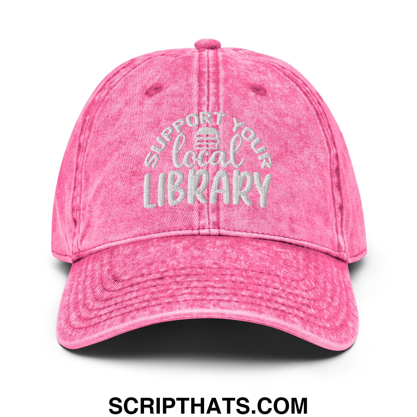 A faded pink denim dad hat with white embroidered support your local library text and a small library icon