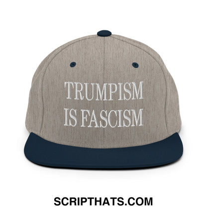 A gray and navy blue snapback hat with white embroidered text reading trumpism is fascism on the front panel
