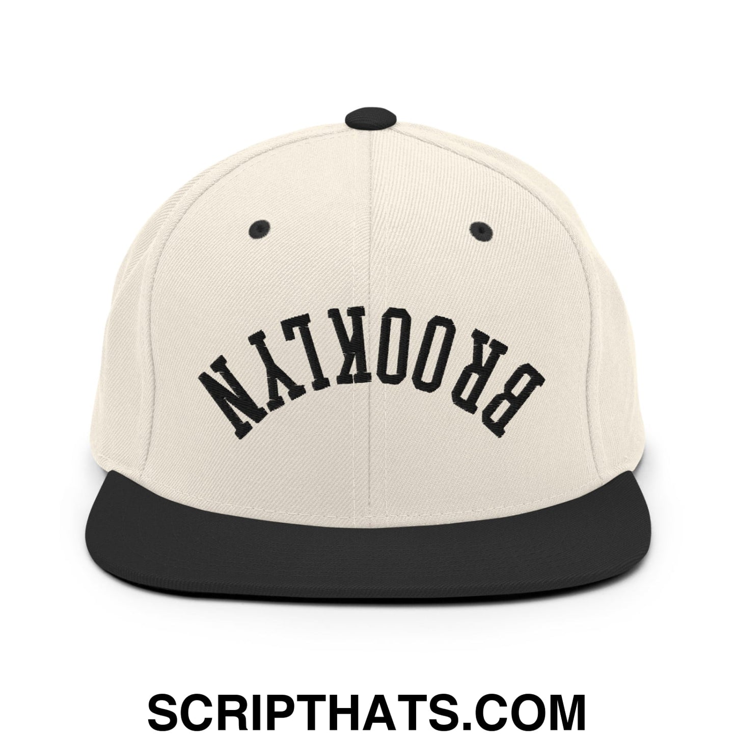 Beige snapback cap with black flat bill brim and upside down brooklyn embroidered in bold arching letters