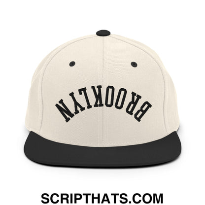 Beige snapback cap with black flat bill brim and upside down brooklyn embroidered in bold arching letters