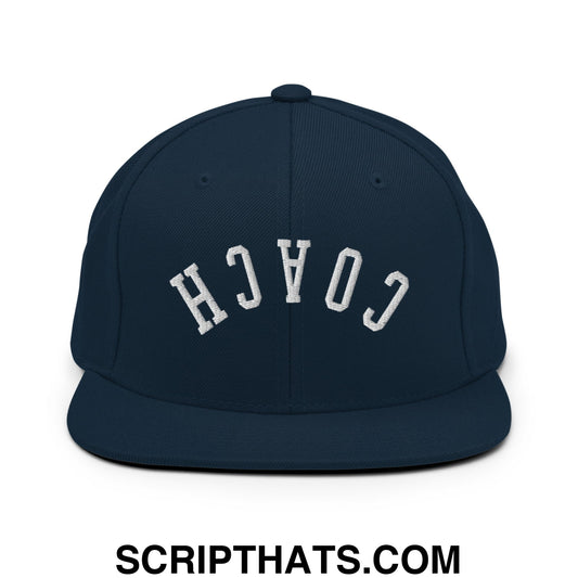 Navy blue snapback hat with white embroidered coach lettering and flat bill brim in an arched design