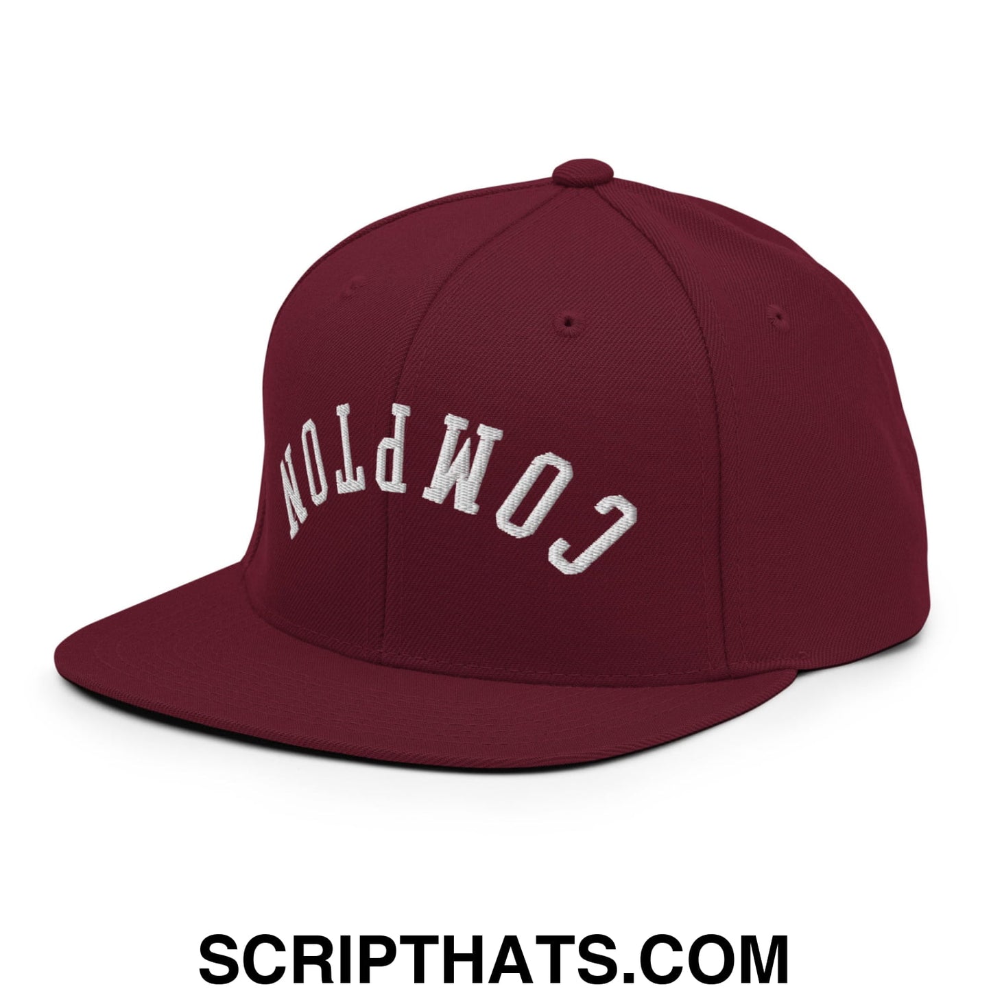 Maroon snapback cap with white embroidered compton lettering and flat bill brim in upside down design