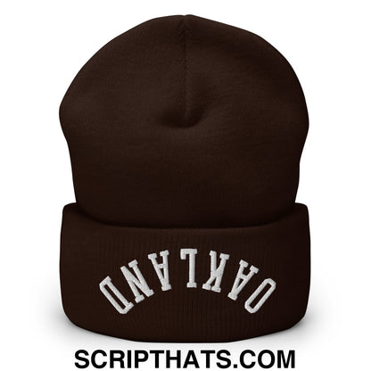 A dark brown knit cuffed beanie embroidered with white upside down oakland text on the folded brim