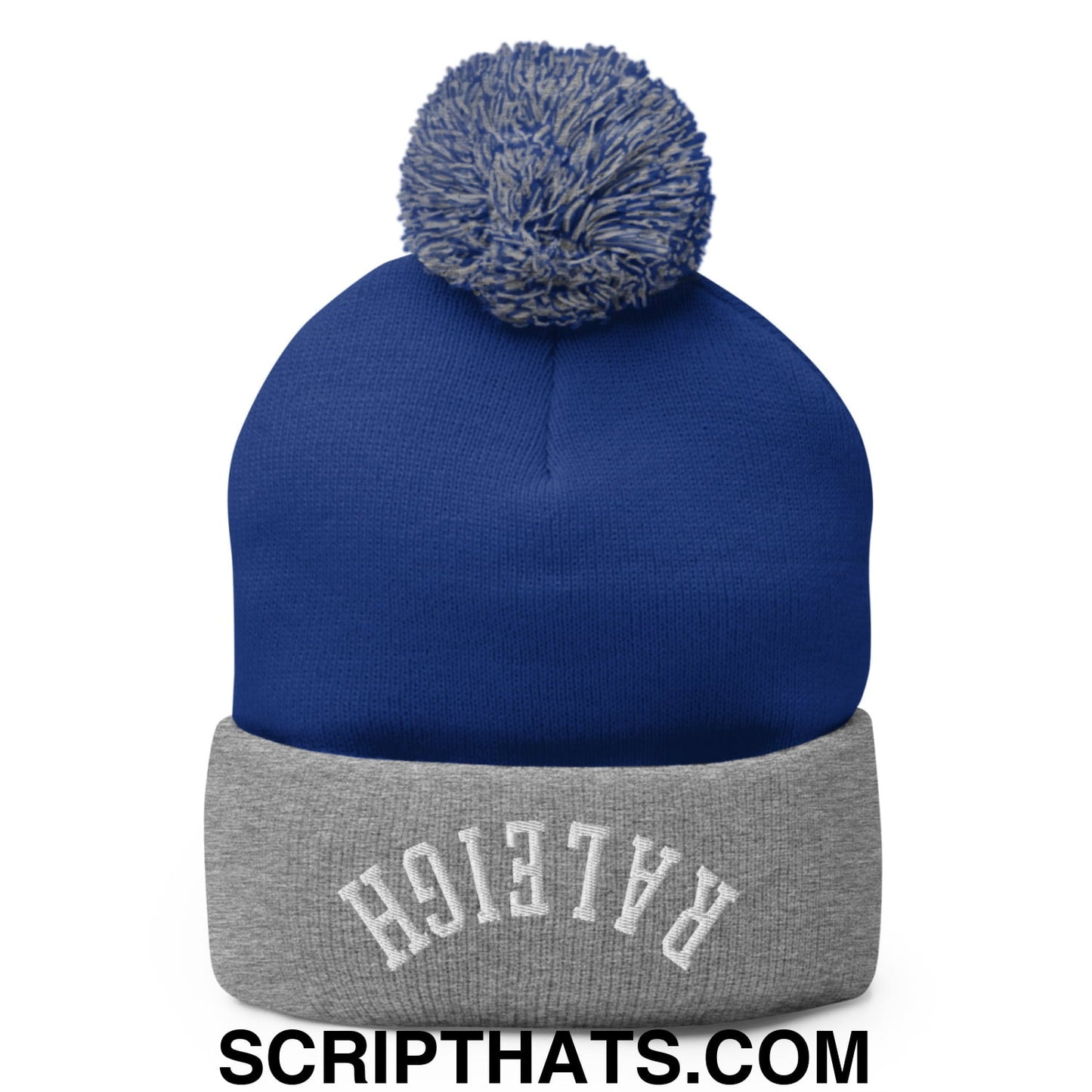 Royal blue knit beanie with gray cuffed brim, white embroidered lettering, and blue-gray pom pom on top