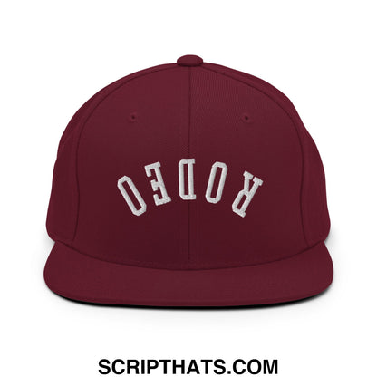 Maroon snapback hat with white embroidered rodeo lettering in an arched design and flat bill brim