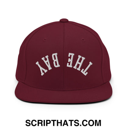 Maroon snapback cap with white embroidered the bay lettering and flat bill brim in upside down design
