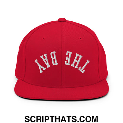 Red snapback cap featuring white embroidered the bay lettering with a flat bill brim for casual streetwear use